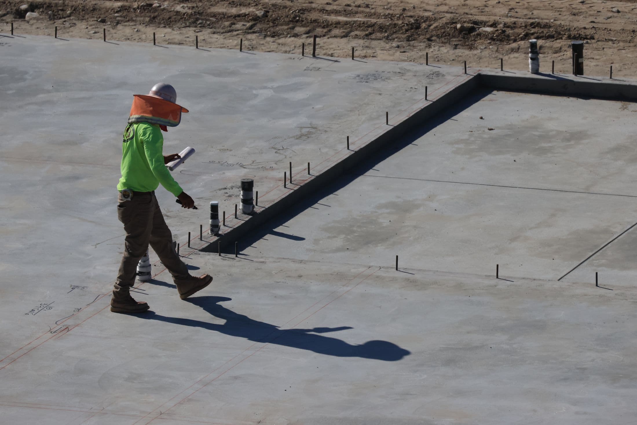 Site engineer inspecting a concrete foundation against construction plans